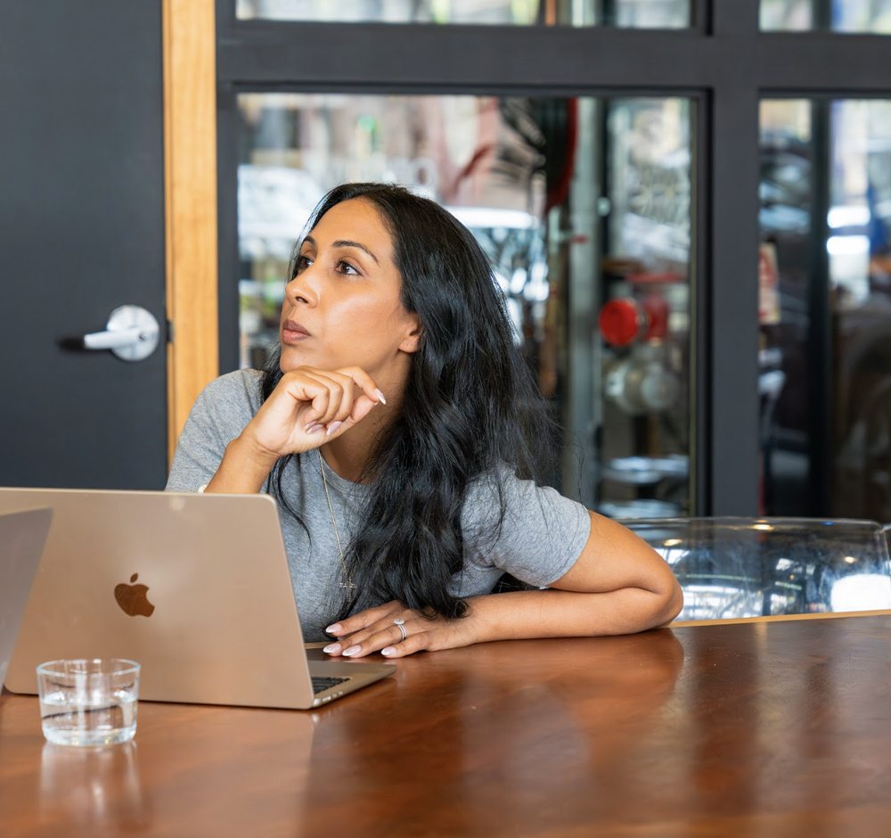 A woman with a laptop in a cafe, thinking about buying her first home